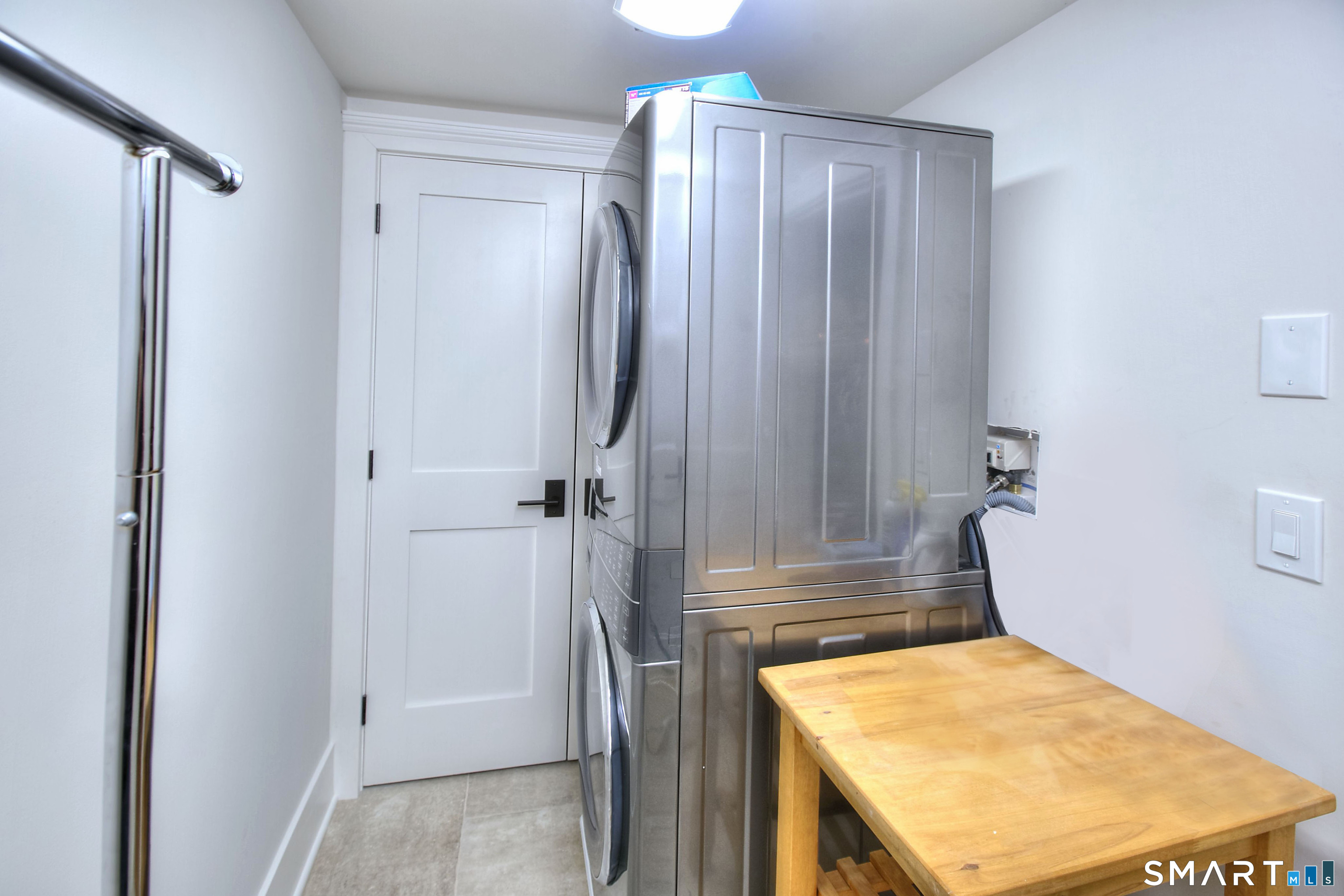 Laundry room with stacked stainless steel washer and dryer beside a wooden folding table.