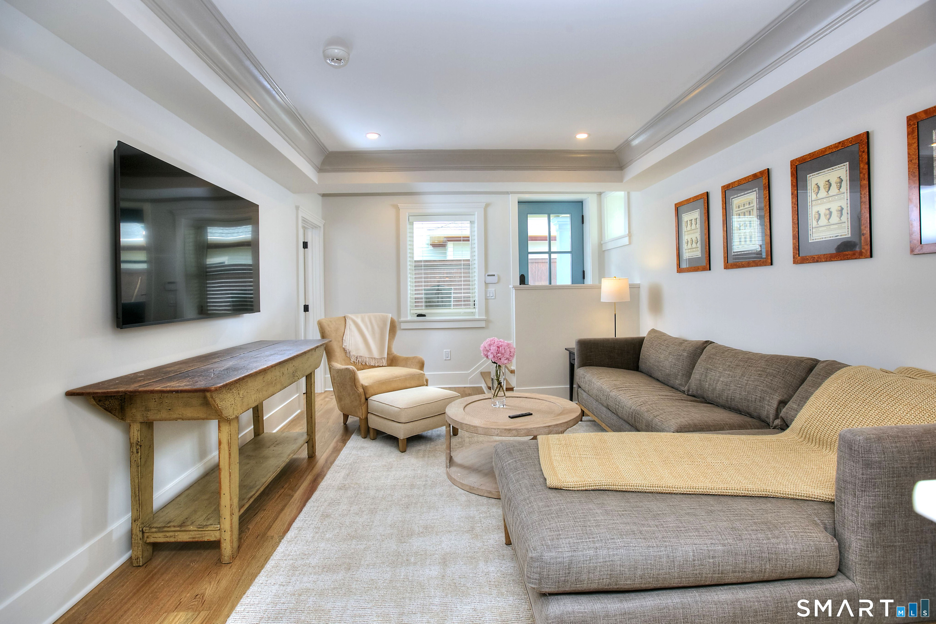 Living room with a gray sectional, tan armchair, round coffee table, and wall-mounted television.