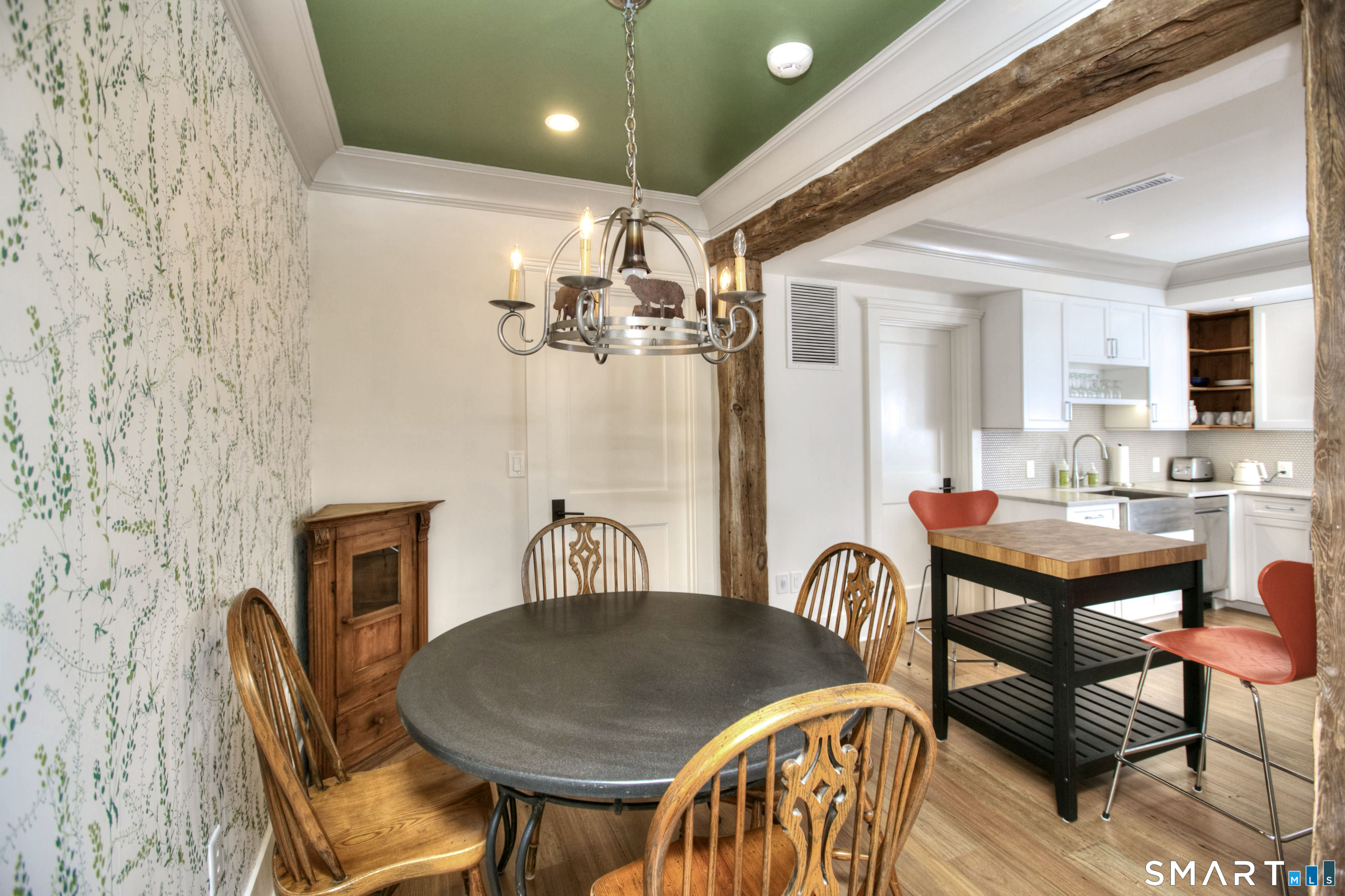 Dining area and kitchen with exposed timber beams, botanical wallpaper, and a butcher-block island.