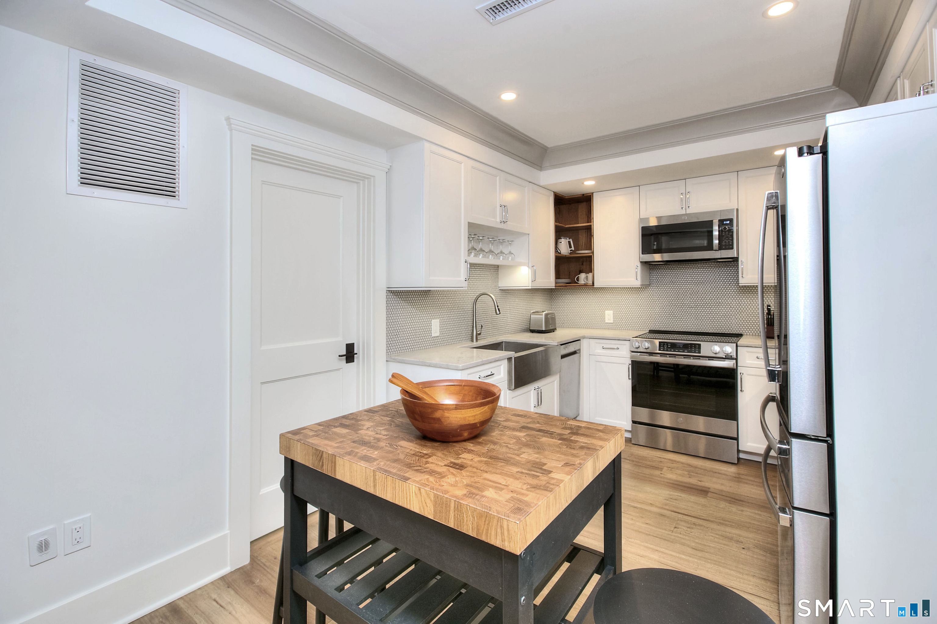Kitchen with white cabinetry, stainless steel appliances, and a butcher-block island topped with a wooden bowl.