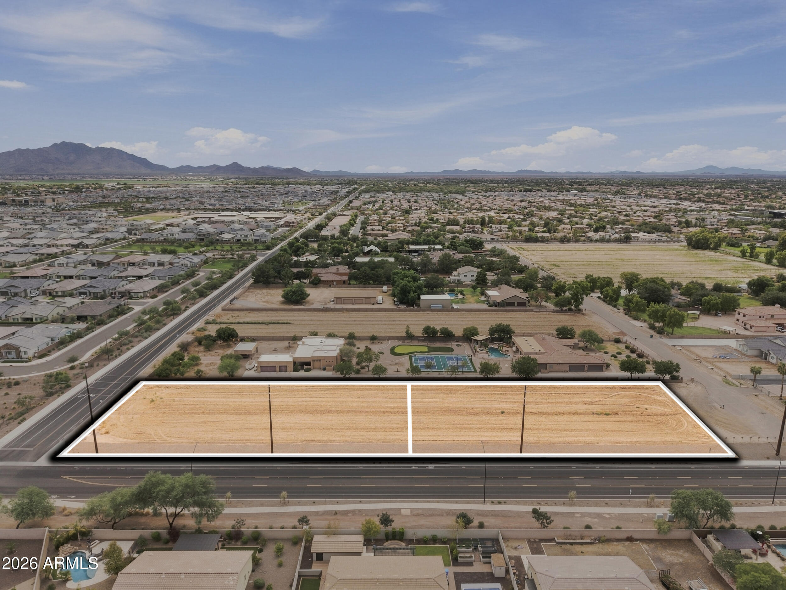 Aerial view of vacant land outlined beside a road, with suburban homes and mountains beyond.