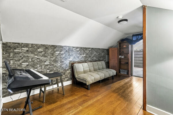 Furnished den with a keyboard, light sofa, stone-pattern accent wall, and hardwood floor.