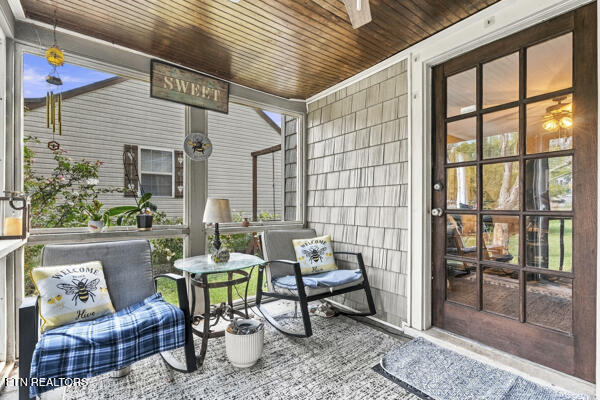 Covered porch with rocking chairs, a glass-top table, and a dark wood-framed glass door.