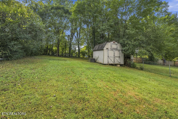 Grassy backyard with a storage shed, fenced lawn, and mature trees.