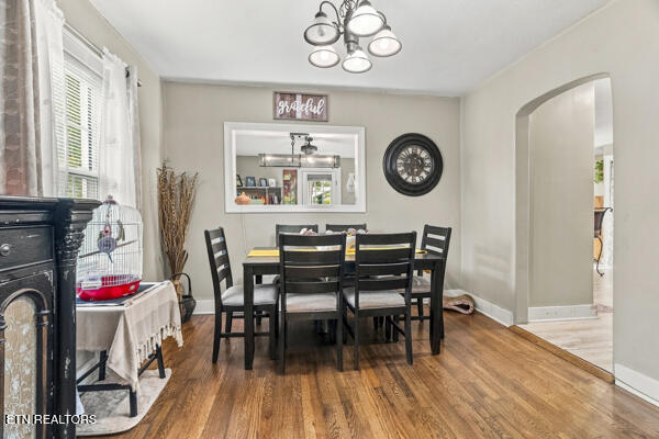 Dining room with a black table and chairs, hardwood floors, chandelier, and arched doorway.