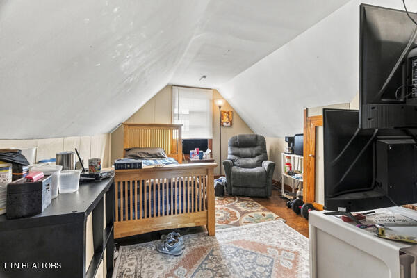 Attic bedroom with a sloped ceiling, wooden bed frame, recliner, and television.