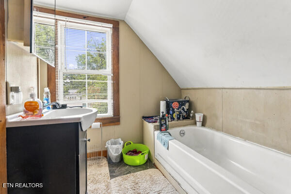 Bathroom with a white bathtub, dark vanity, and window beneath a sloped ceiling.