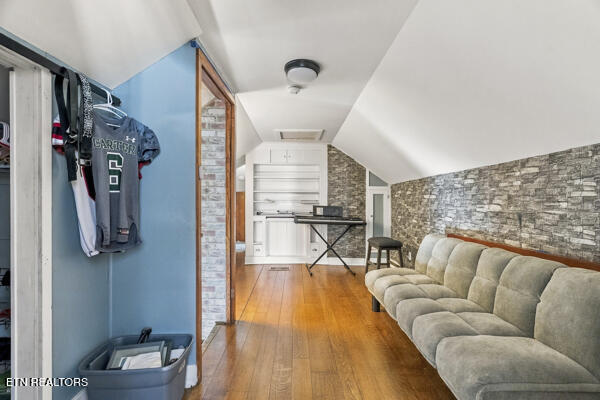 Living area with a beige sectional, stone accent wall, hardwood floors, and a compact kitchenette.