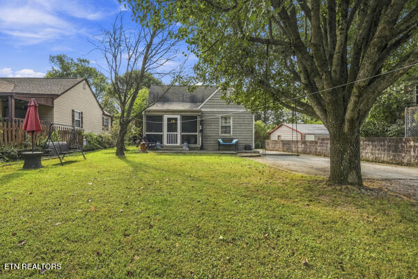 Backyard of a gray single-story home, with a broad lawn, mature trees, and a small deck.