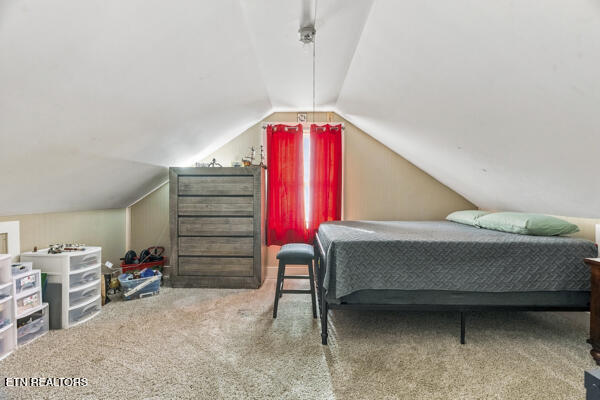 Attic bedroom with a gray bed beneath a sloped ceiling and bright red curtains.