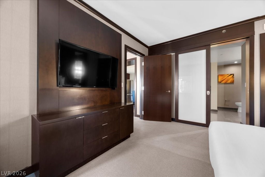 Bedroom with a wall-mounted TV, dark wood cabinetry, and an open bathroom doorway.
