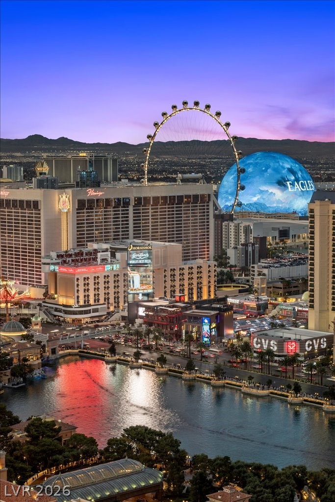 Las Vegas Strip at dusk, with the High Roller and Sphere above illuminated hotels and reflective water.