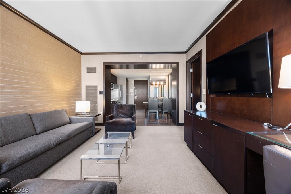Furnished living room with gray sofa, glass coffee tables, and dark wood TV wall; dining area beyond.