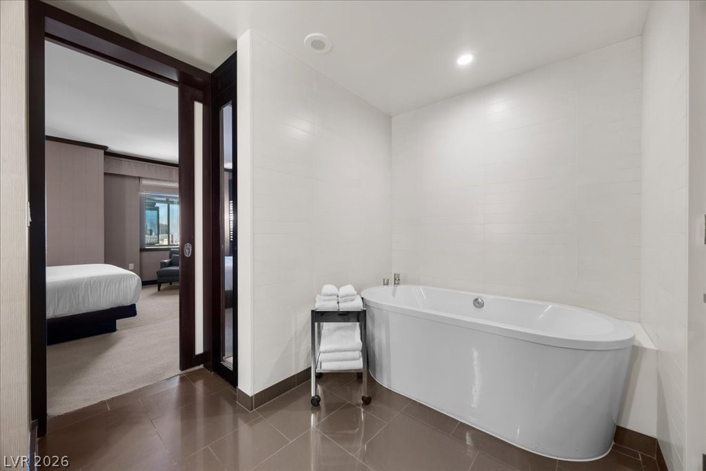 Bathroom with a large white bathtub and folded towels beside an open doorway to a bedroom.