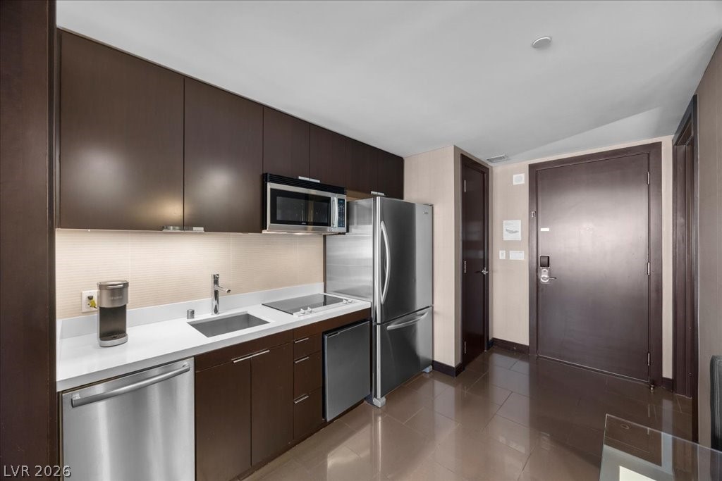 Compact kitchen with dark cabinetry, white counters, and stainless-steel appliances beside the entry door.