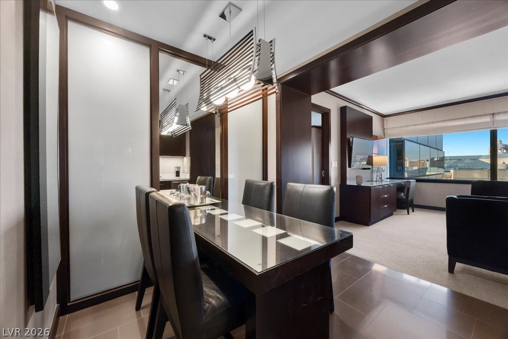 Dining area with a glass-top table and dark leather chairs beside large windows.