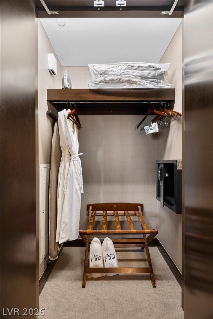 Closet with an Aria robe and slippers, wooden luggage rack, hangers, and wall-mounted safe.