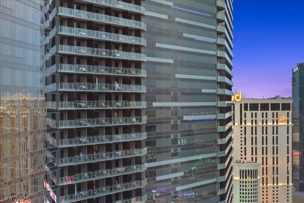 Glass high-rise with stacked balconies at dusk, beside a hotel with an illuminated “ph” sign.