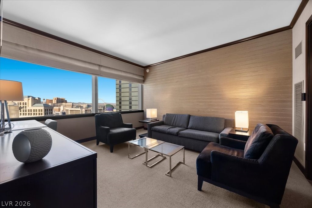 Living room with a gray sofa and dark armchairs beside large windows overlooking the city.