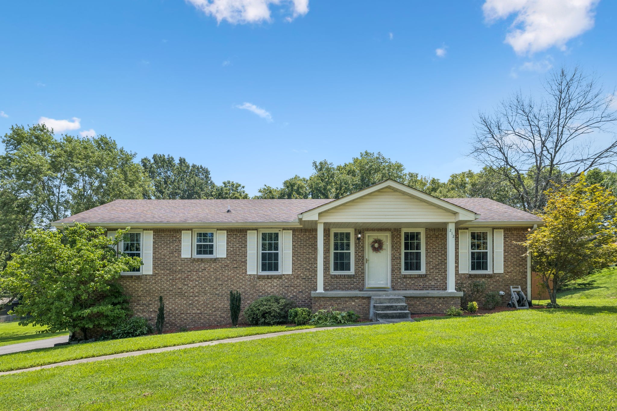 Single-story brick ranch house with a covered entry, front steps, and a broad green lawn.