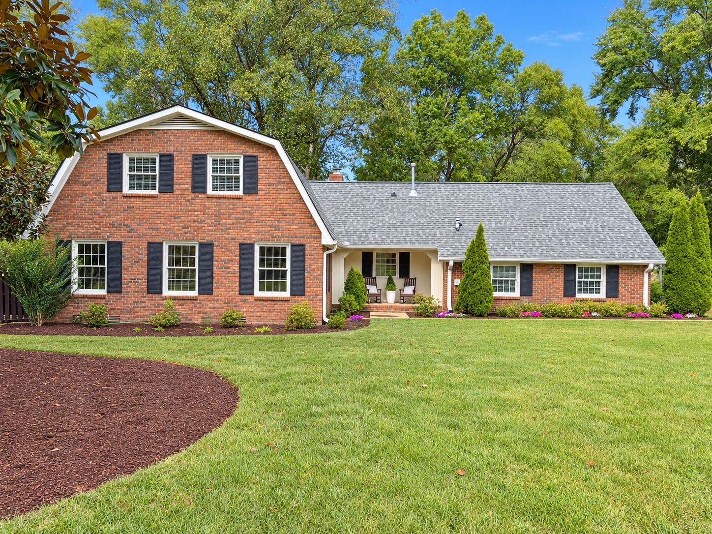 Two-story brick house with dark shutters, a covered porch, and a landscaped lawn.