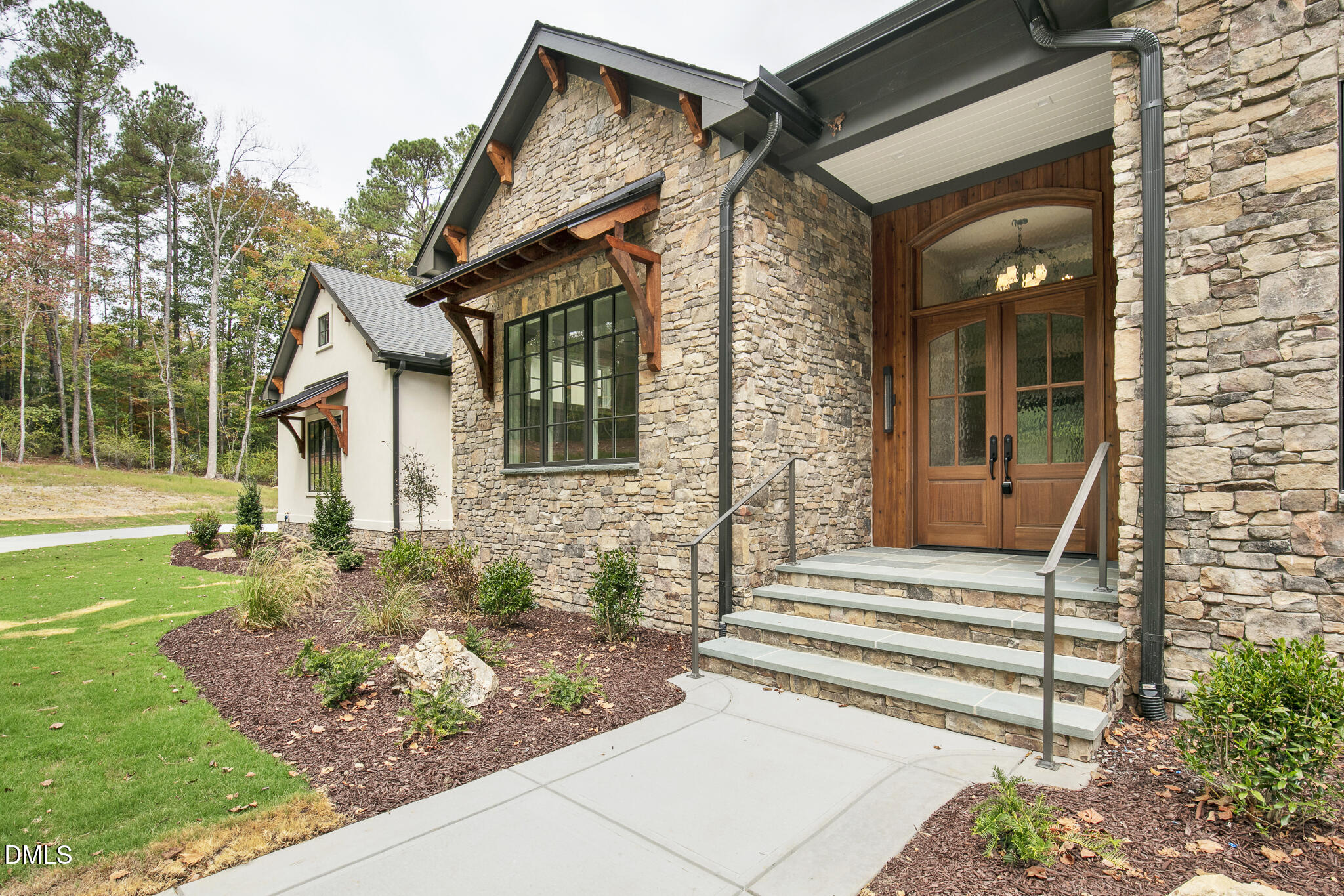 Stone-and-stucco home with a timber-trimmed entry, wooden double doors, and landscaped front yard.