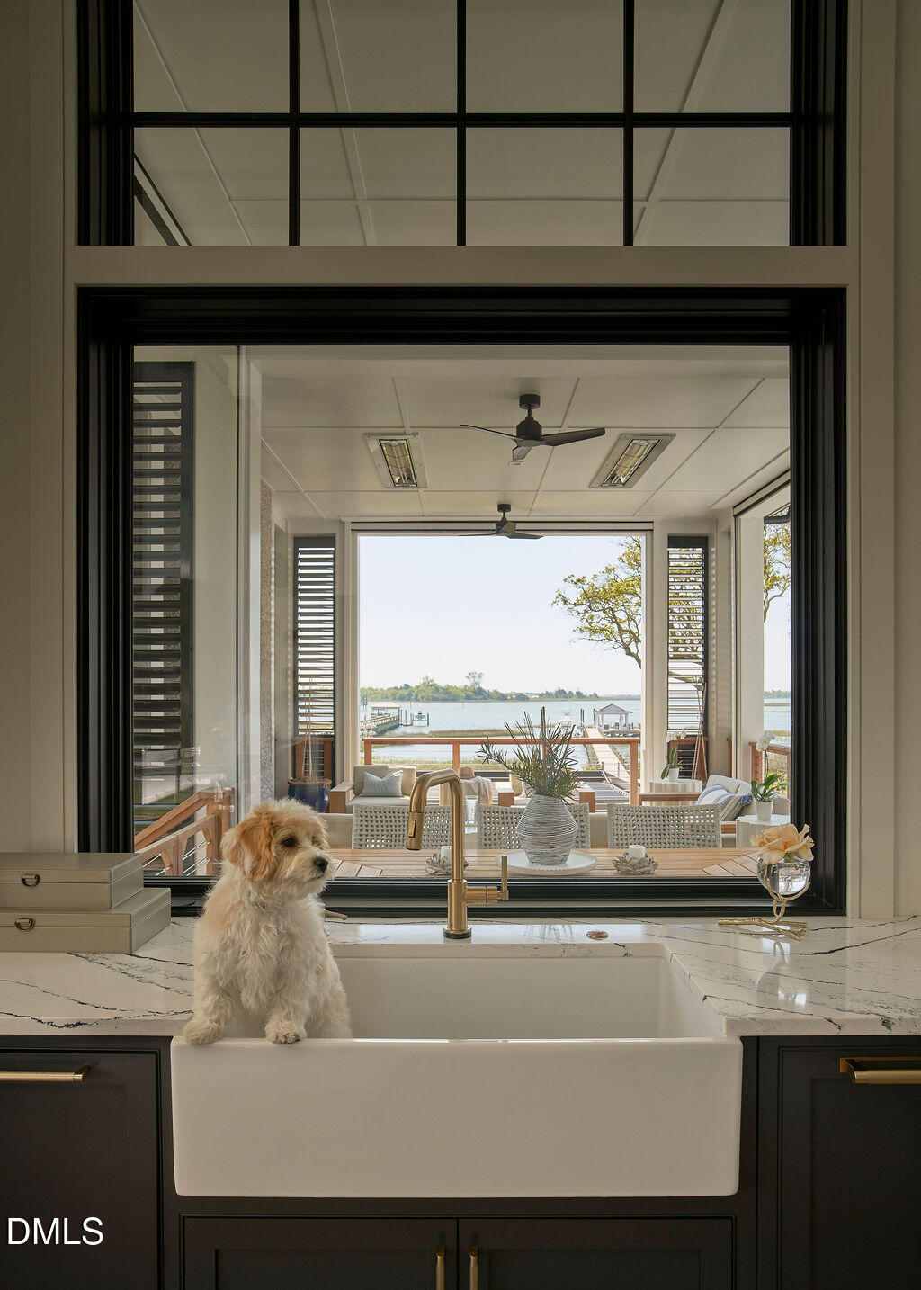 Kitchen sink and small dog by a large window overlooking a covered porch and lake.