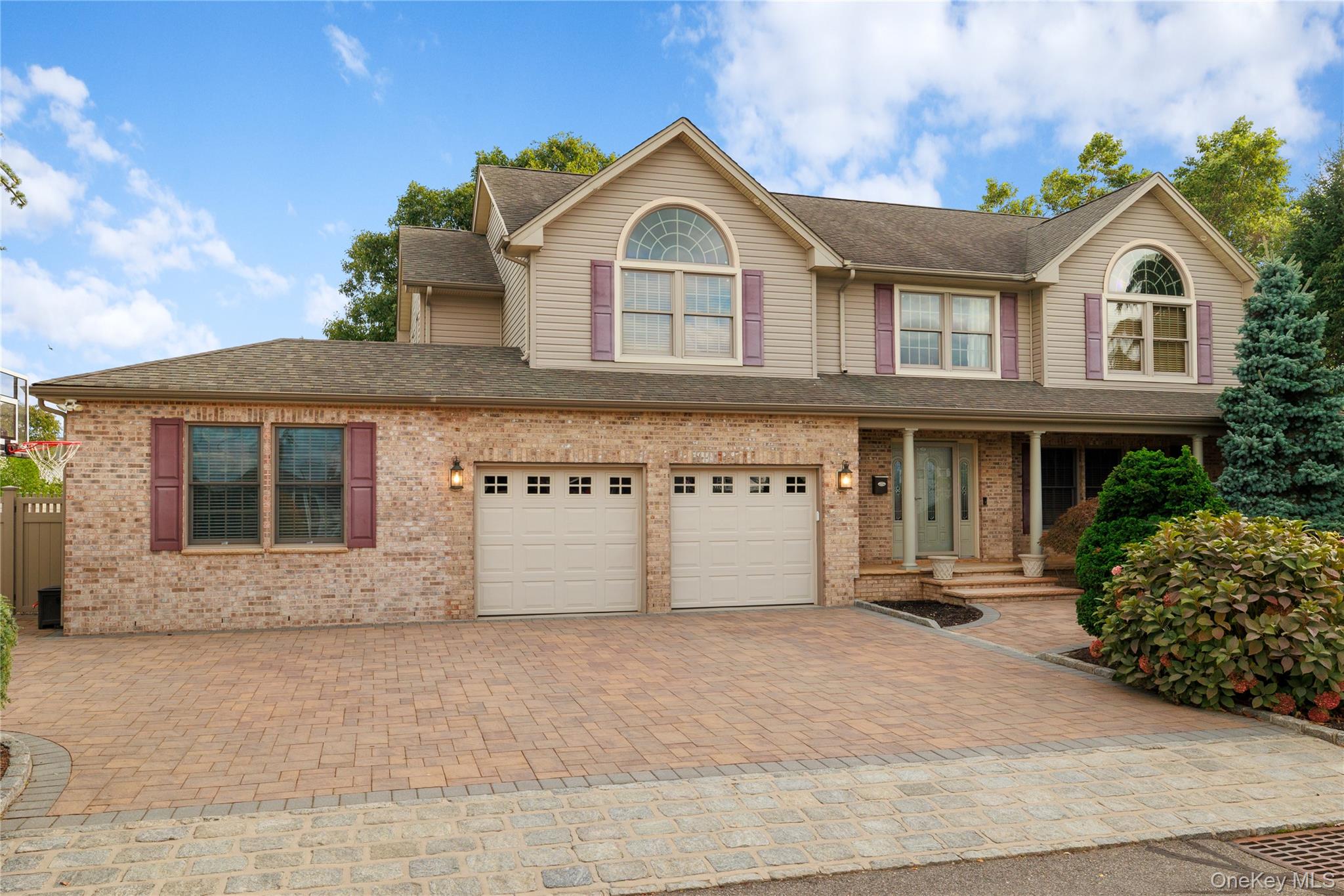 Two-story brick and beige house with two garage doors, arched windows, and a broad paved driveway.