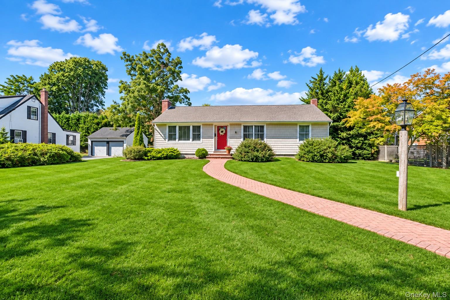 Single-story house with a red front door, curved brick walkway, and broad green lawn.