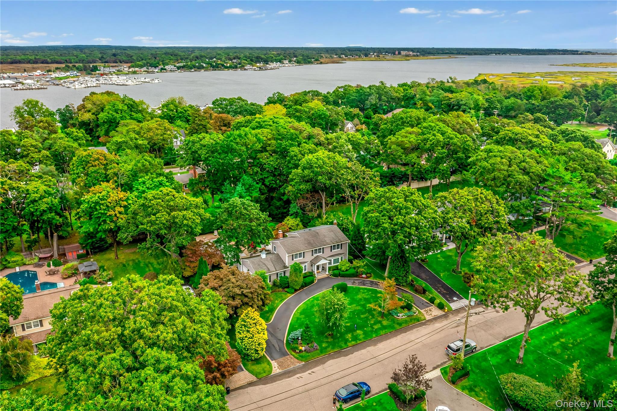 Aerial view of a tree-lined South Shore neighborhood beside a bay, with a landscaped home and swimming pool.