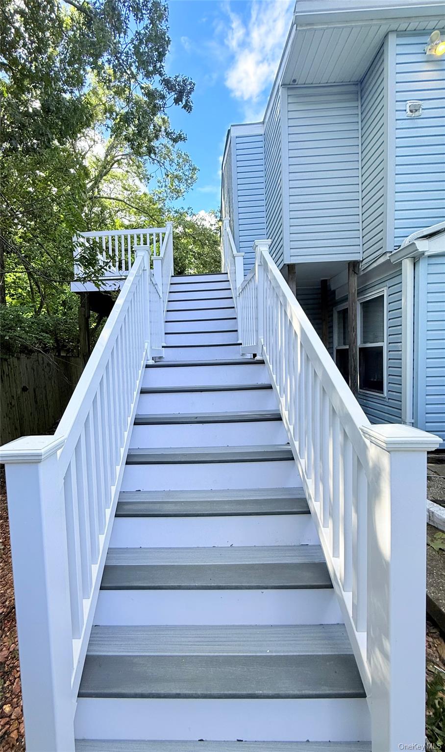 White-railed staircase leading to a landing beside a light blue-sided building.