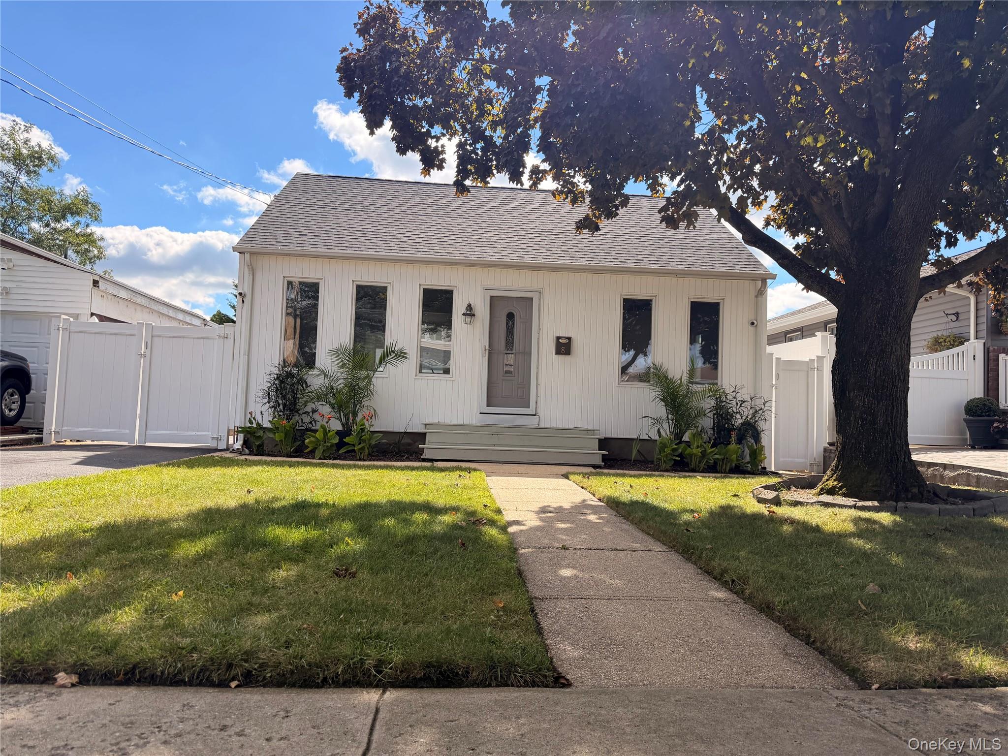 Small white office building with a front walkway, fenced yard, and large shade tree.