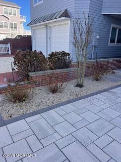 Blue-gray coastal house with white double garage doors, gravel landscaping, and a broad paved walkway.