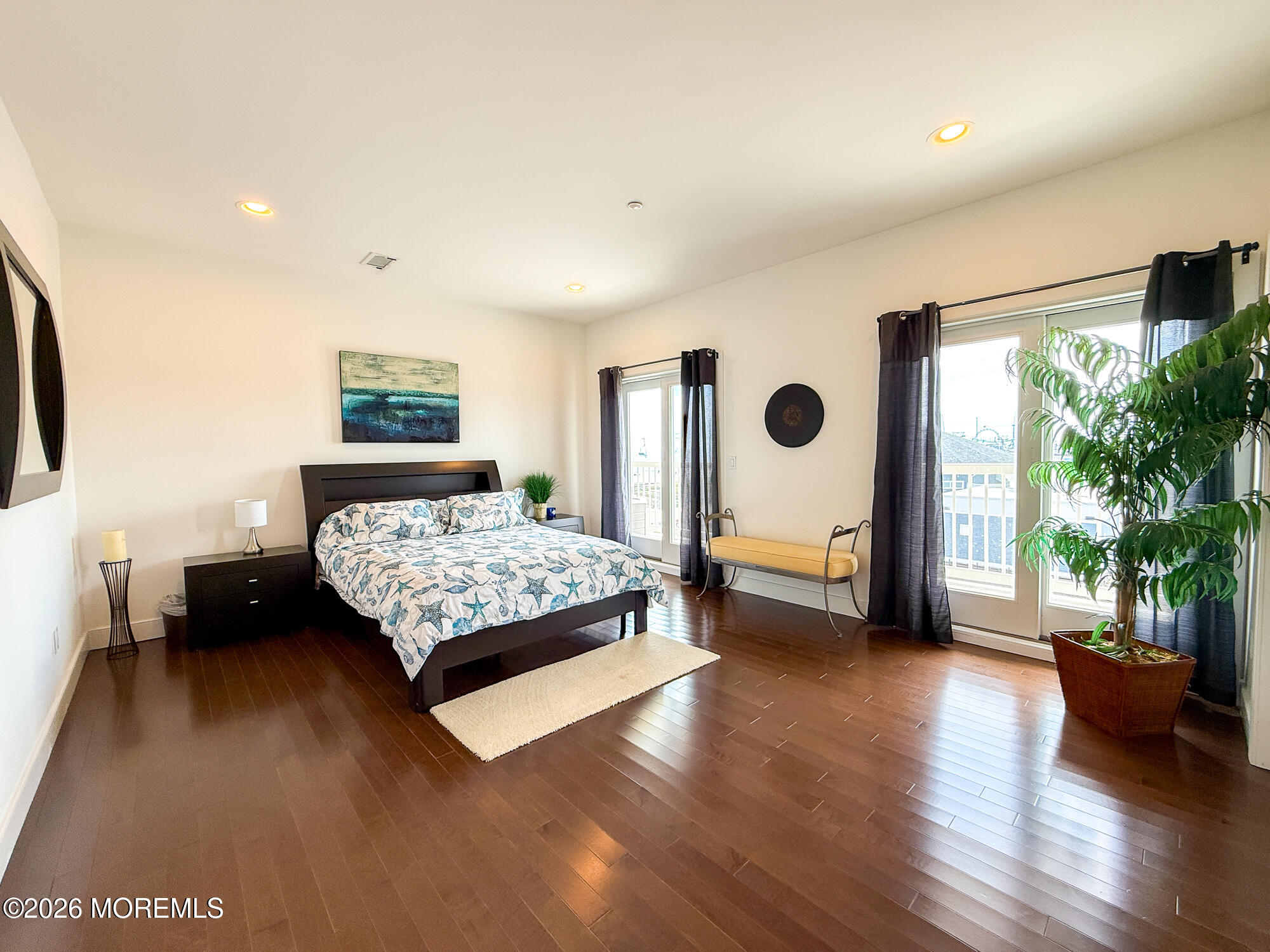 Furnished bedroom with blue sea-life bedding, dark hardwood floors, and tall windows opening onto a balcony.