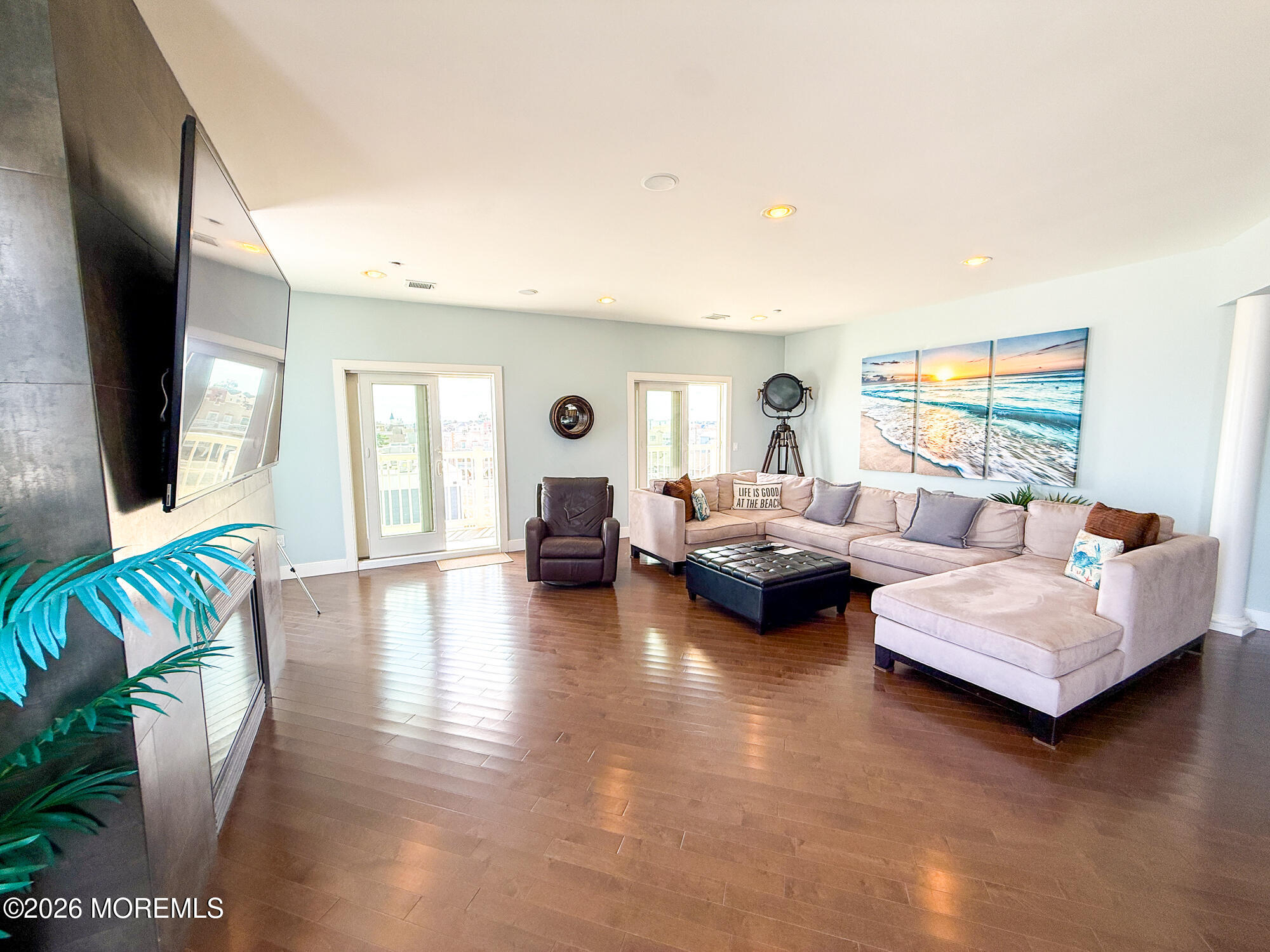 Living room with a pale sectional, dark wood floors, and beach-sunset artwork.