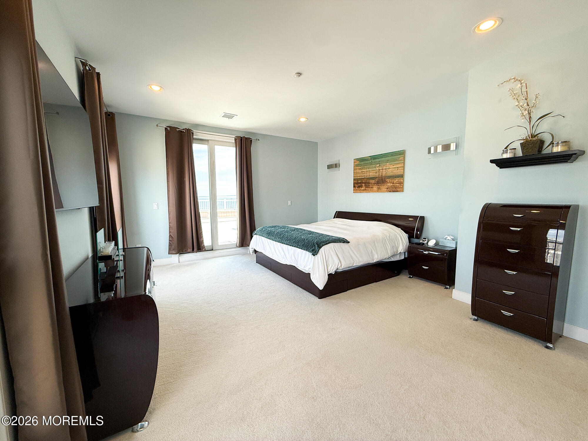 Furnished bedroom with dark wood furniture and sliding glass doors opening to a balcony.