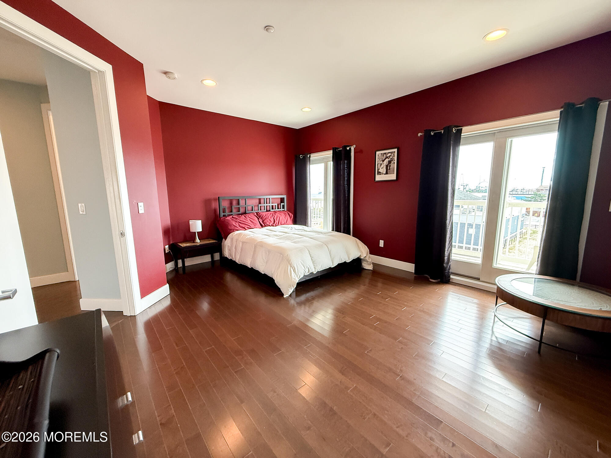 Bedroom with red walls, dark wood floors, and glass balcony doors.