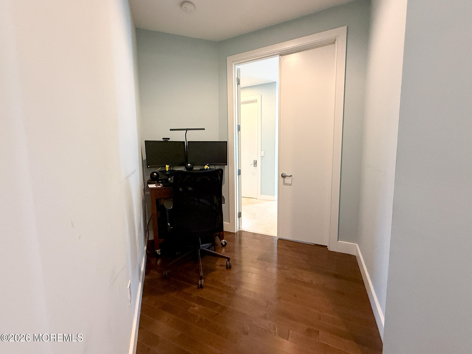Home office with a two-monitor desk, rolling chair, and dark hardwood floors.