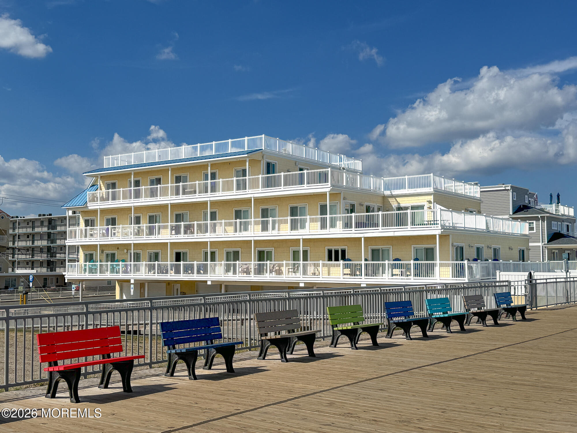 Seaside condominium with stacked white-railed balconies behind colorful boardwalk benches.
