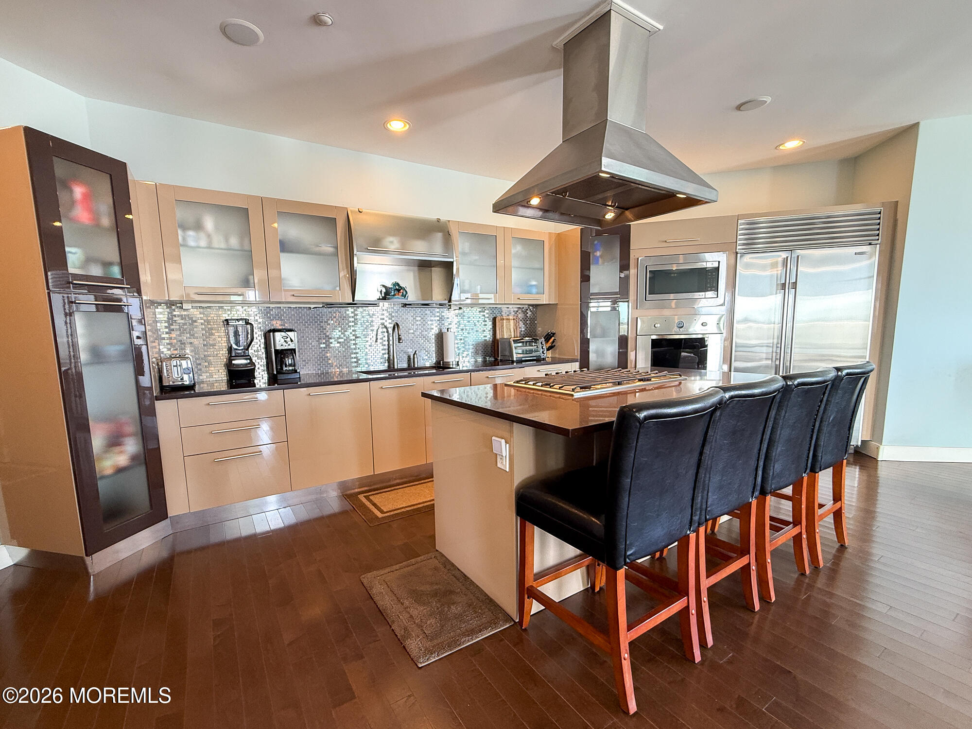 Modern kitchen with stainless steel appliances and an island cooktop lined with four bar stools.