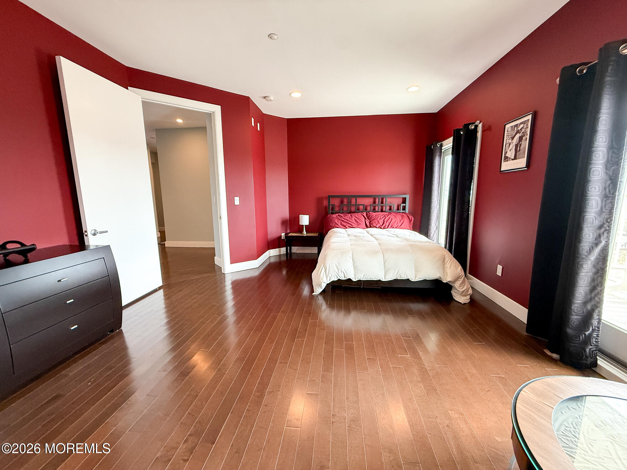 Furnished bedroom with deep red walls, hardwood floors, and a dark metal bed frame.
