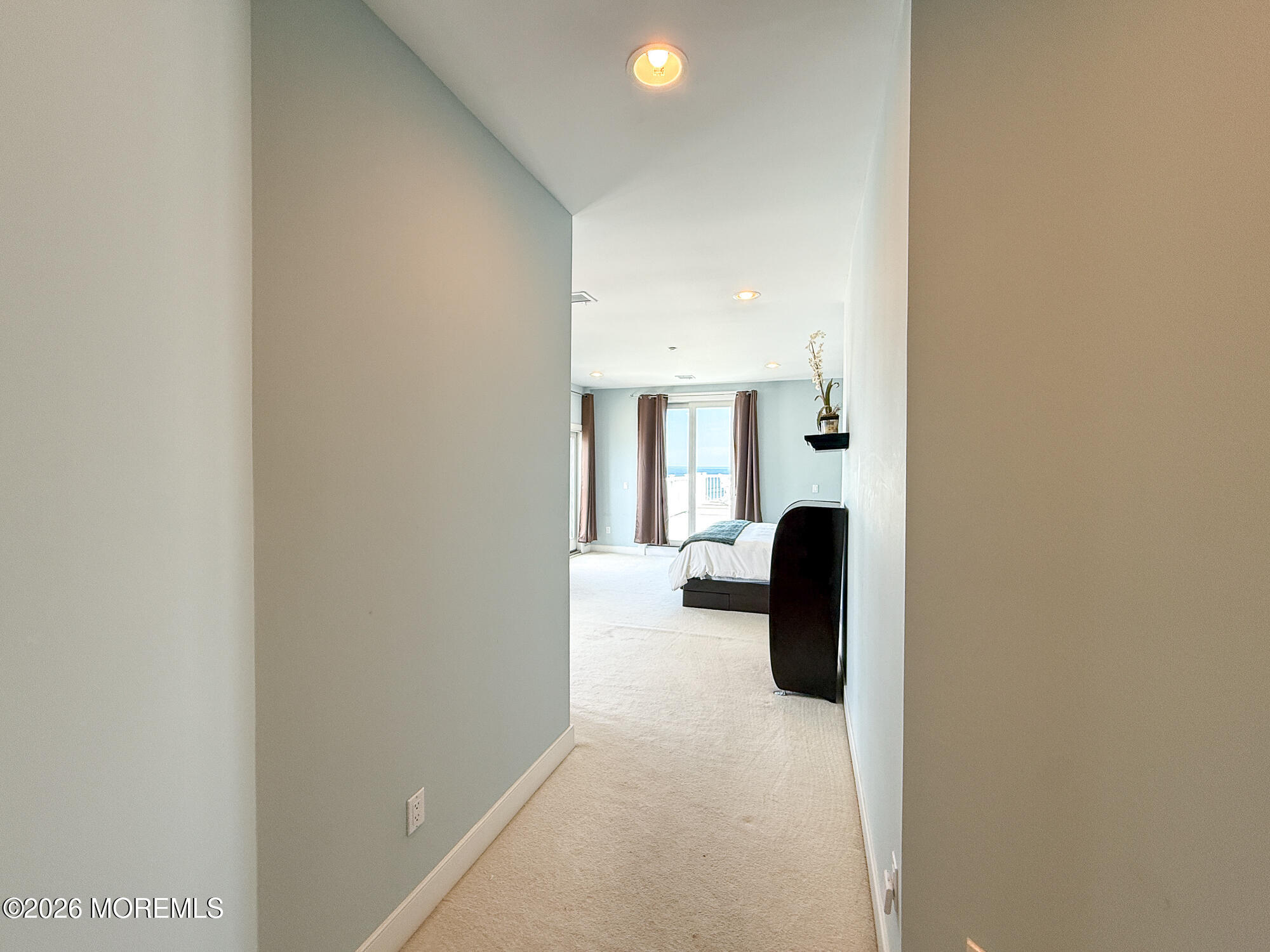 Bedroom at the end of a carpeted hallway, with balcony doors and an ocean view.