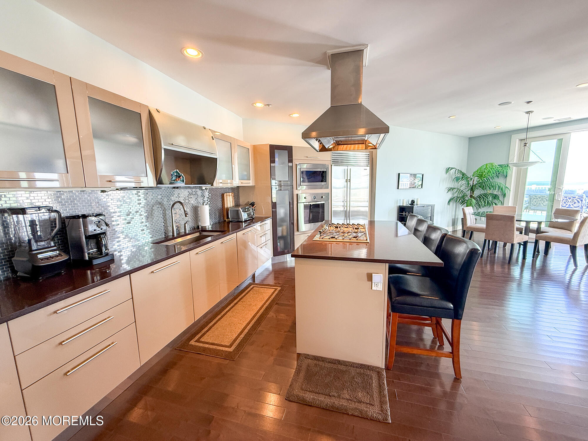 Modern kitchen with stainless appliances, a gas cooktop island, and ocean visible through the balcony doors.