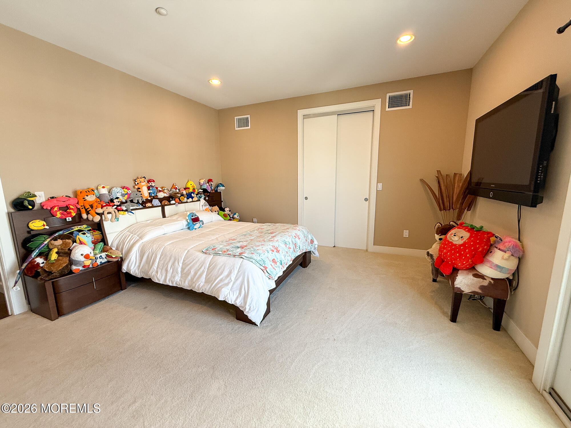 Bedroom with white bedding, floral throw, plush toys, and a wall-mounted television.