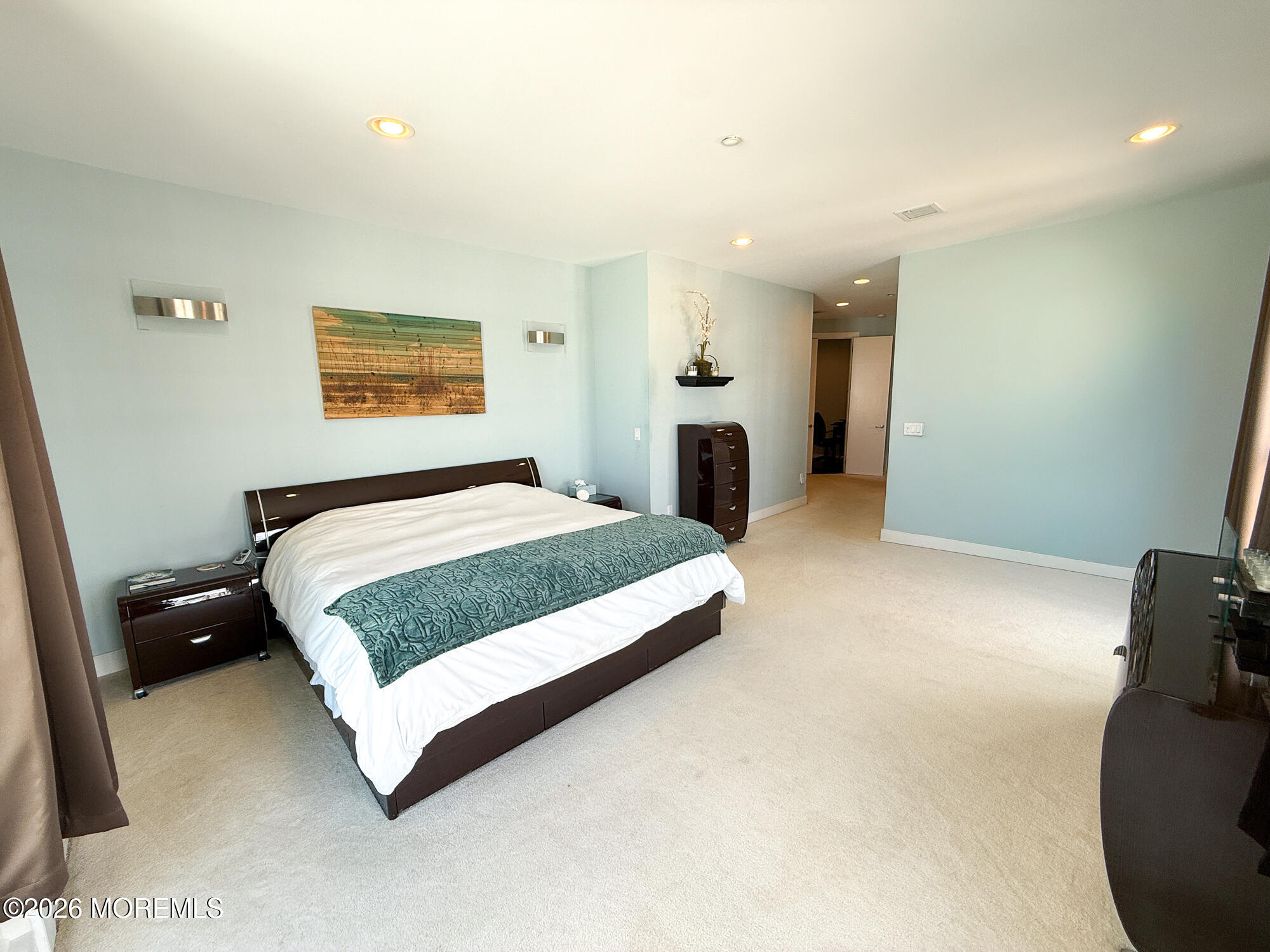 Furnished bedroom with a dark wood bed, teal patterned throw, pale blue walls, and beige carpet.