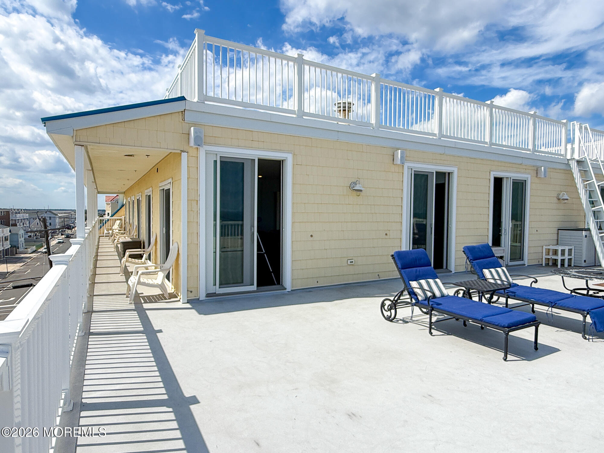 Rooftop deck with blue lounge chairs, white railings, and sliding doors along a pale yellow residence.