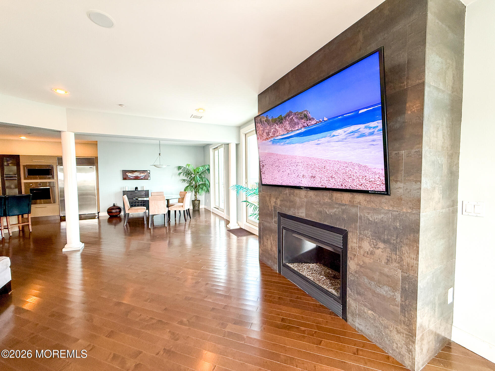 Open-plan living and dining area with hardwood floors, a tiled fireplace, and a large wall-mounted television.