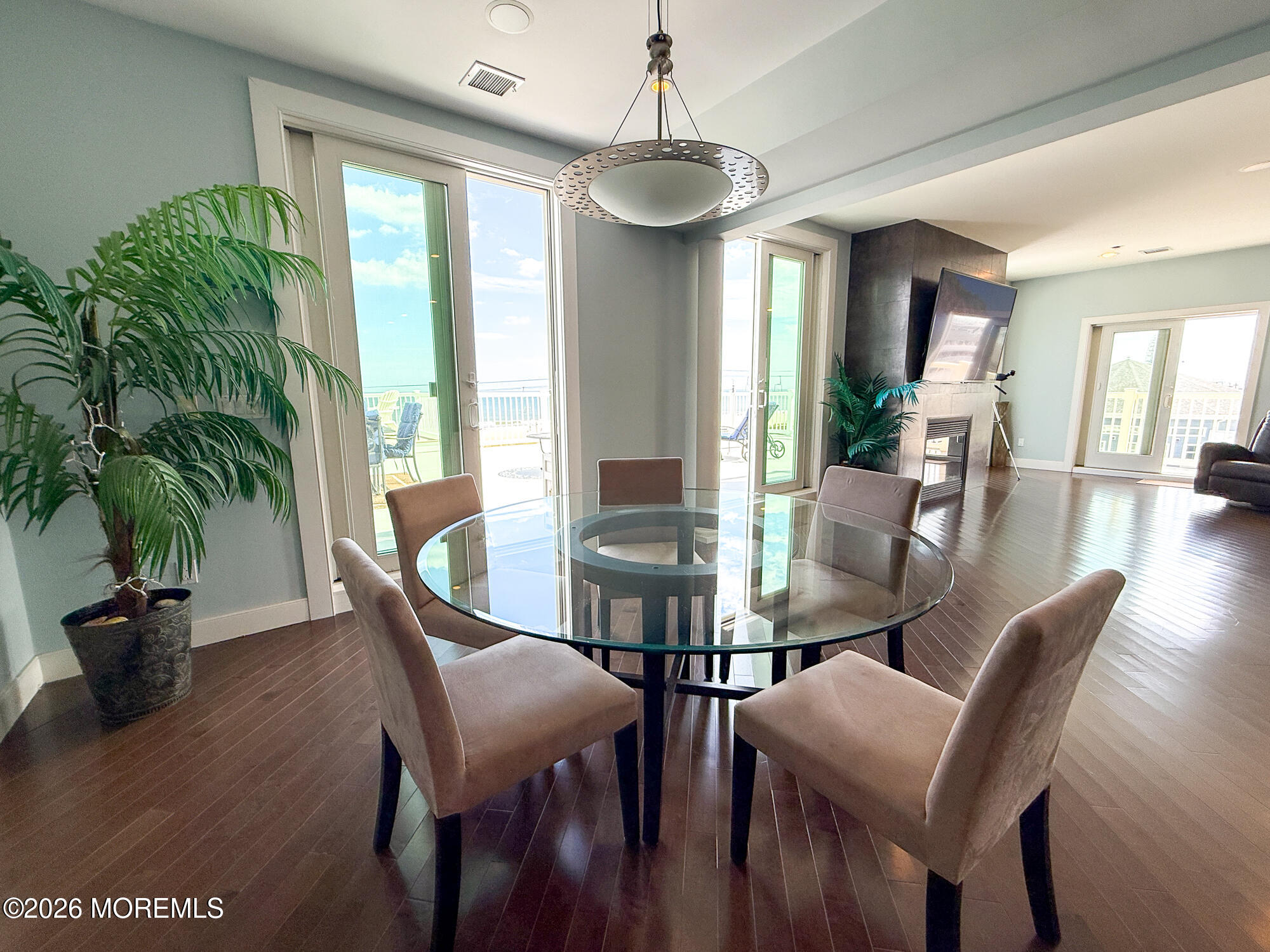 Dining area with a round glass table, ocean-facing balcony doors, and an adjoining living room with a fireplace.