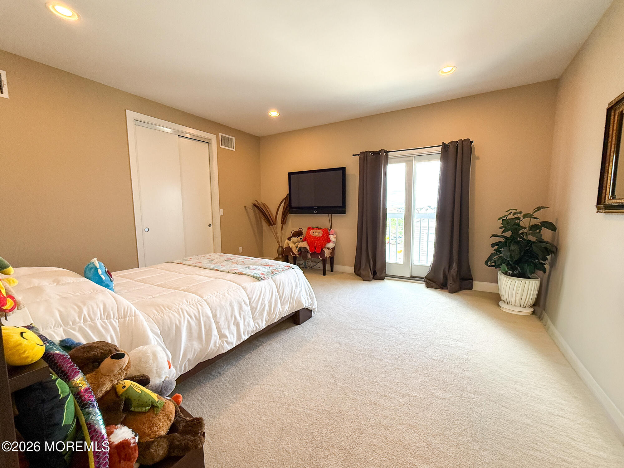 Furnished bedroom with a white bed, stuffed toys, and sliding glass doors.