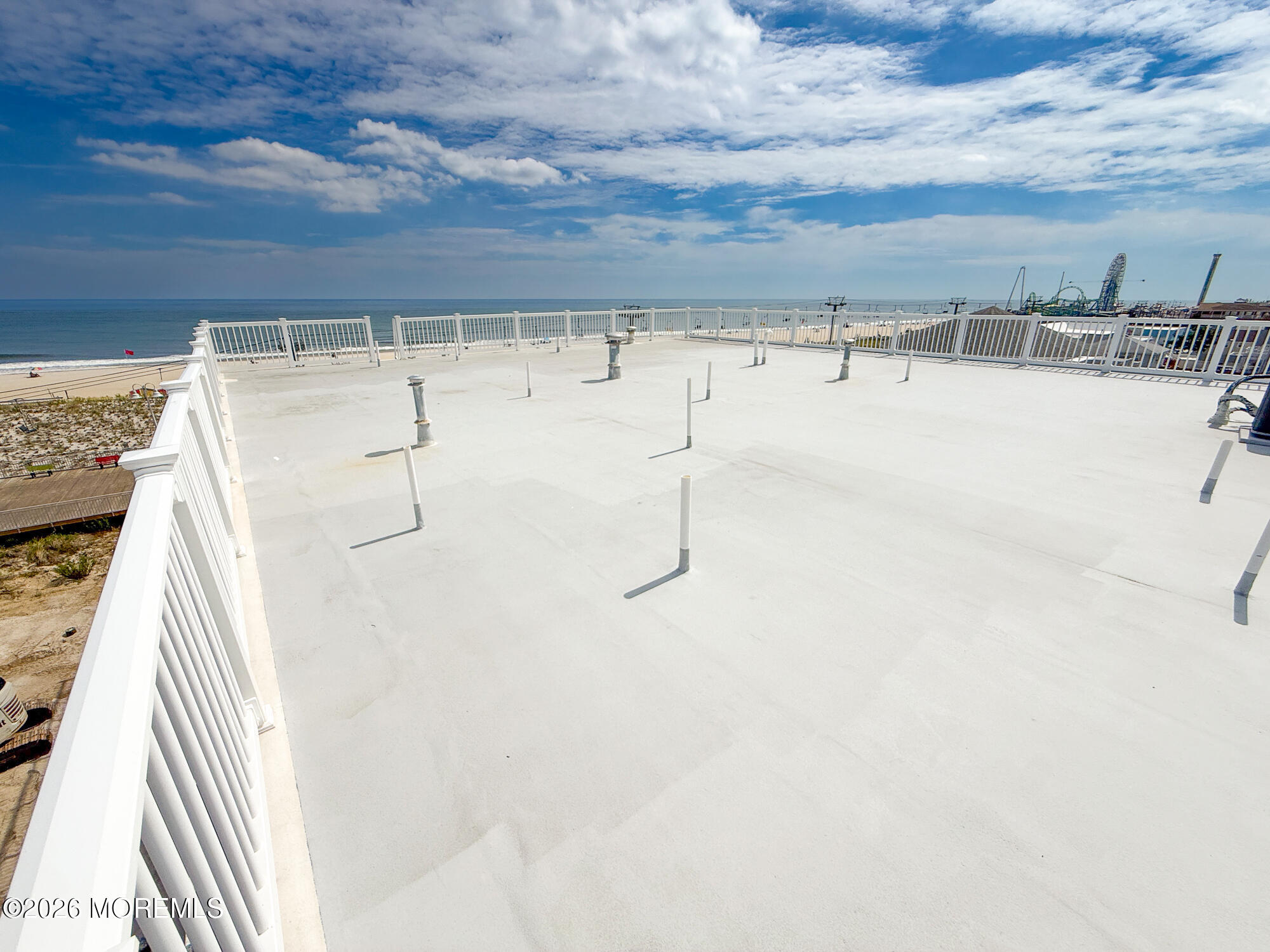 Oceanfront rooftop terrace with white railings and distant amusement park rides.